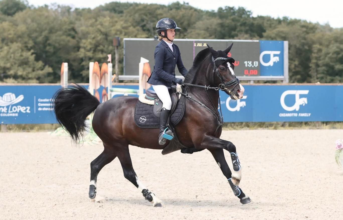 Jeune cavalier au galop sur son poney noir, en finale de concours de saut d'obstacles