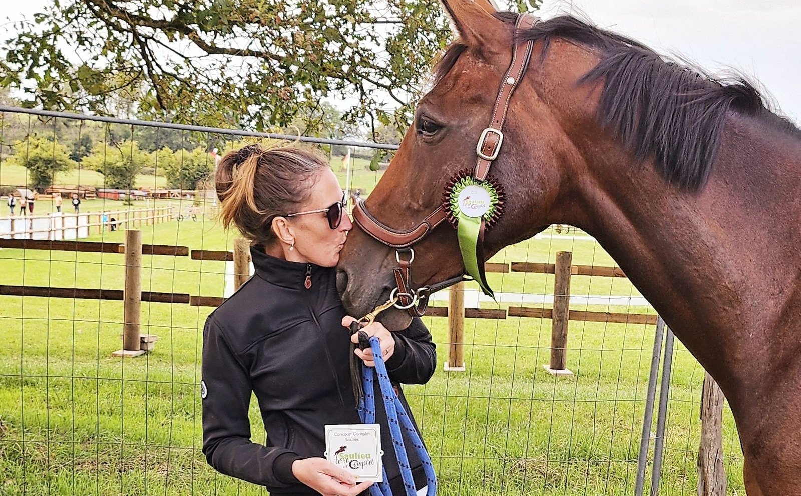 Kelly van Delft debout au pré, la main sur l'encolure de son cheval bai