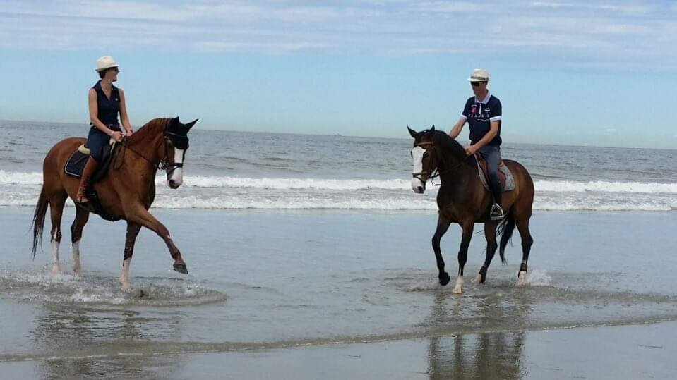 Kelly et Marc-André van Delft à cheval côte à côte dans les vagues, sur une plage