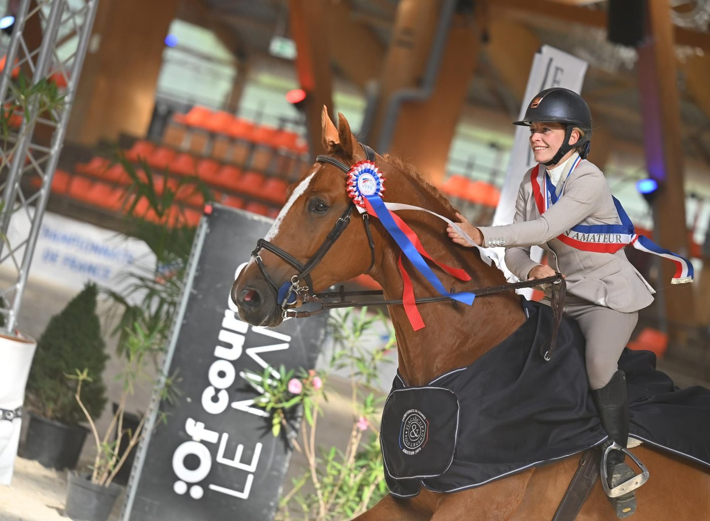 Cavalière avec son écharpe de championne sur son cheval alezan portant un flot