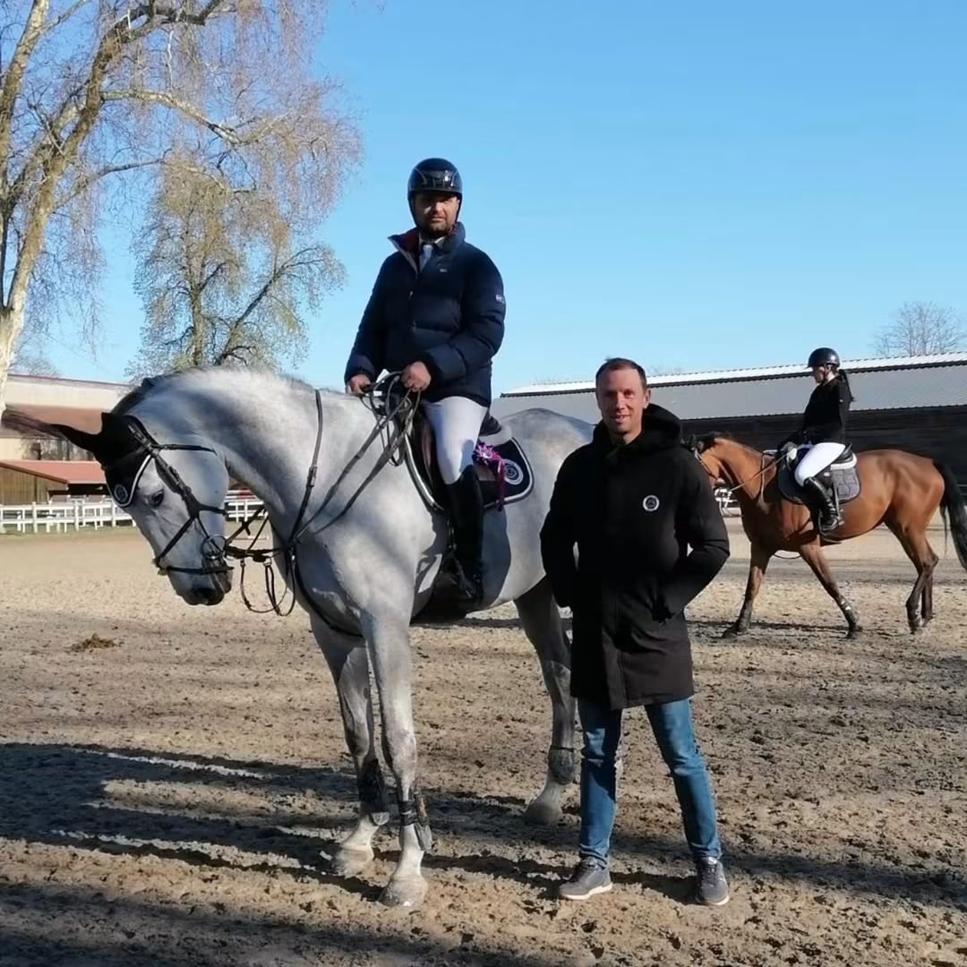 Cavalier sur un cheval gris en carrière, avec son coach à pied