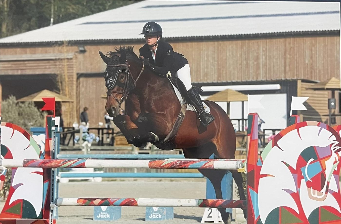 Cavalière en plein saut sur un cheval bai, en concours de saut d'obstacles