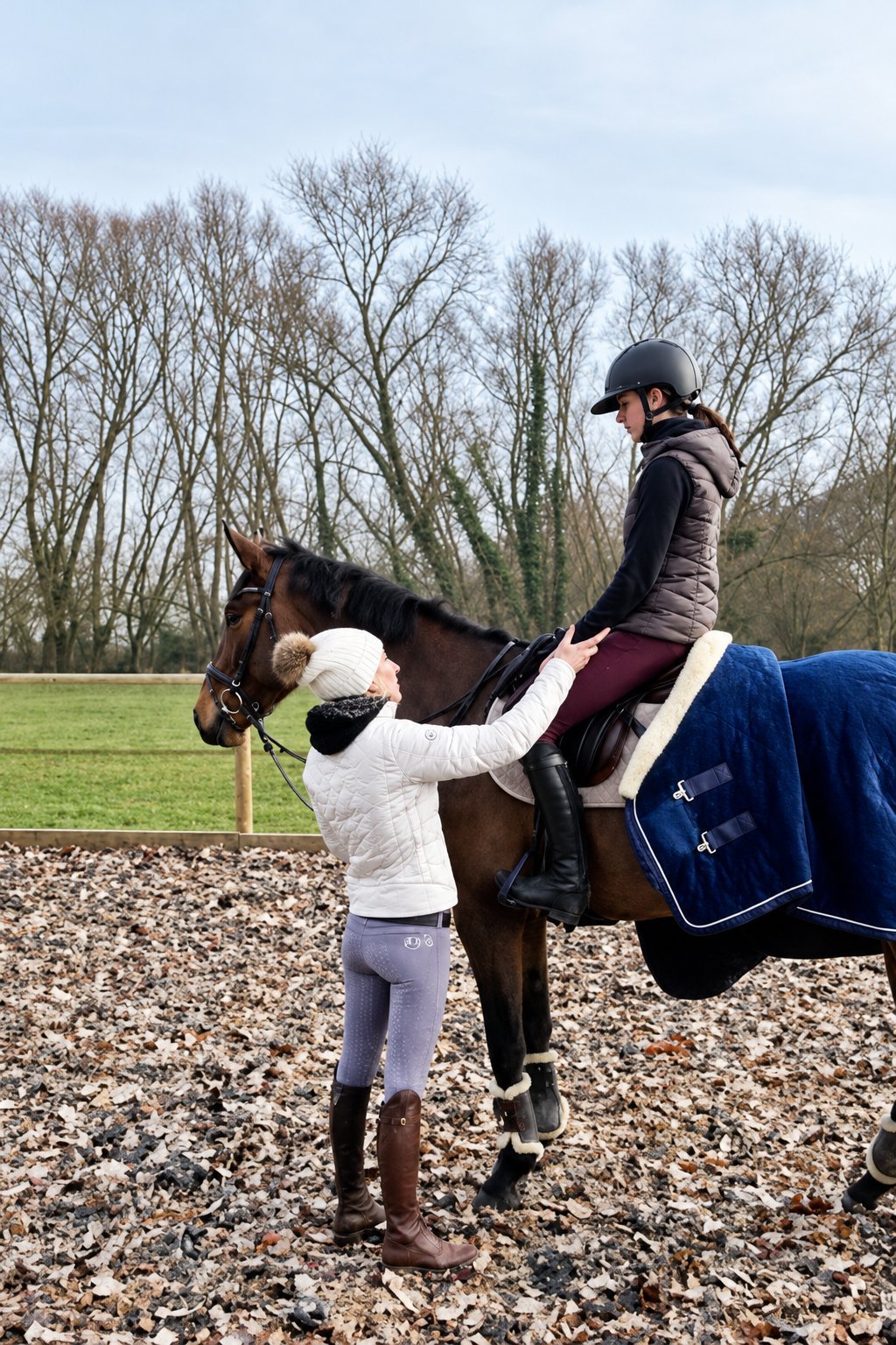 Séance d'hiver en carrière : la coach, à pied, ajuste la position d'une cavalière à cheval